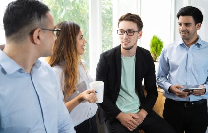 Positive interns sharing training impression. Cheerful young coworkers drinking coffee and chatting. Coffee break or career start concept